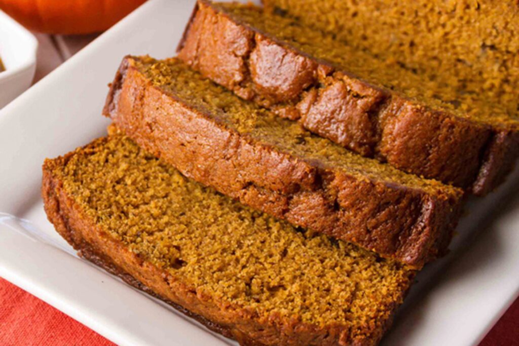 Freshly baked gluten-free pumpkin bread on a cutting board, surrounded by cinnamon sticks and pumpkin slices.